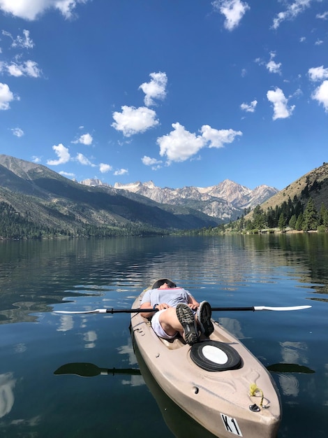 Foto donna sdraiata su un kayak in un lago contro le montagne