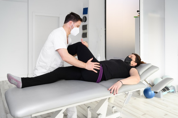 Woman lying on massage table while his physical therapist doing special exercises for physical therapy for sciatica and pinched nerve problems.