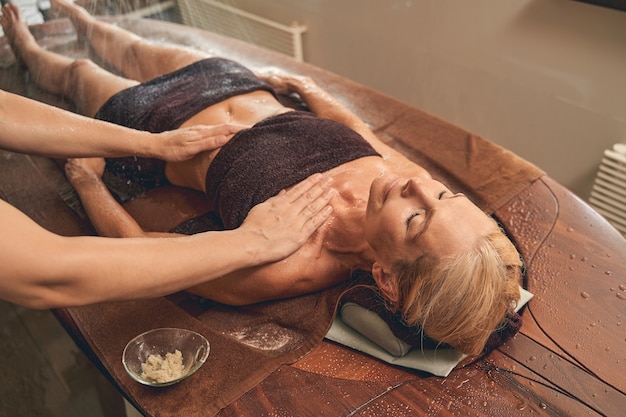 woman lying on the massage table while taking skin care under shower rain