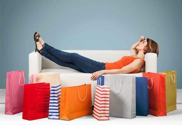 Фото Женщина, лежа на диване за рядом сумок, устала после покупок