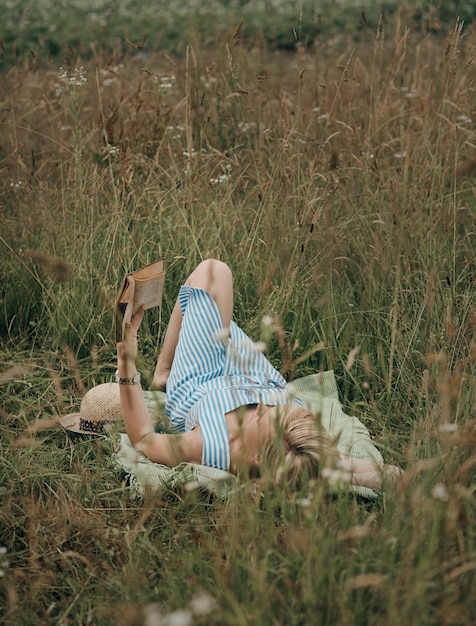 Woman lying on plaid in field and enjoying reading books