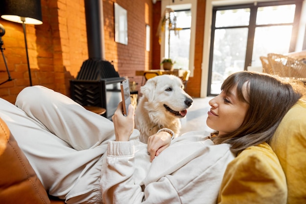 Foto donna sdraiata rilassata su un divano e usando il telefono trascorrendo del tempo con il cane a casa