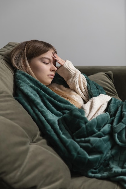 A woman lying on a sofa has a headache and she touches her forehead