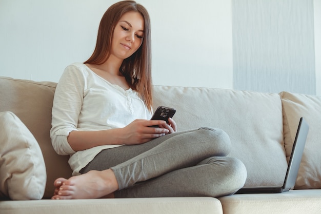 自宅のソファに横になってスマートフォンを手に持っている女性