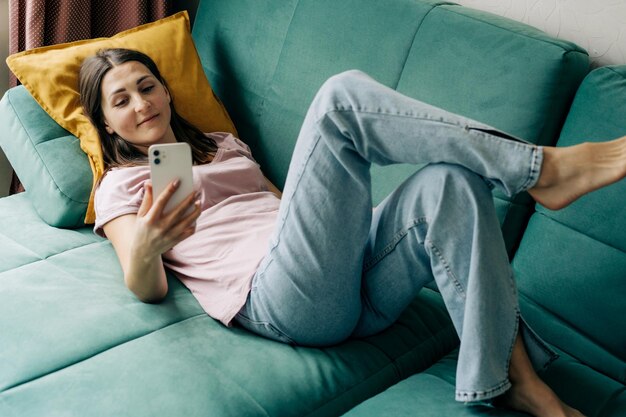 Photo a woman lying on a sofa uses a phone for video calling