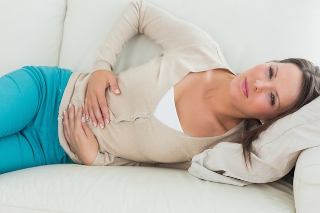 Foto donna sdraiata sul divano con mal di stomaco