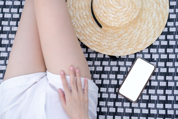 携帯電話とビーチの空白の白い画面で日光浴のベッドに横たわっている女性。