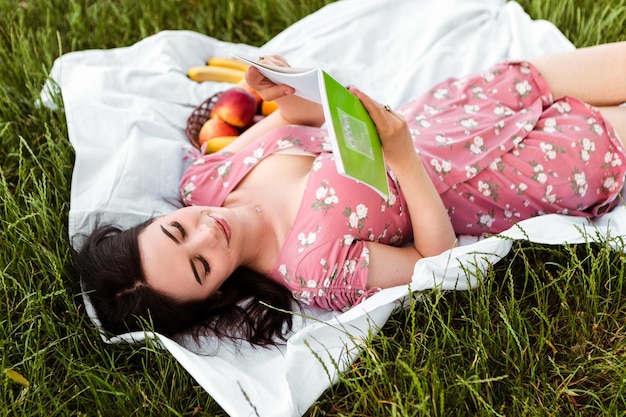 Woman lying on white bedsheet, reading book, smiling