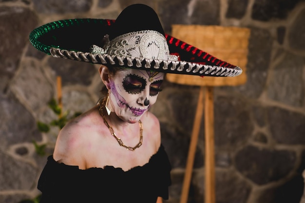 Woman made up as catrina wearing mariachi hat. Mexican woman celebrating day of the dead. Indoor portrait