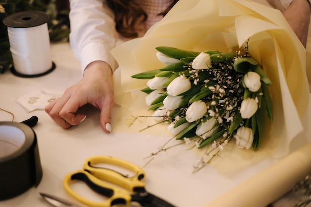 Woman make spring bouquet female florist wrapping beautiful bouquet of spring flowers in pack paper