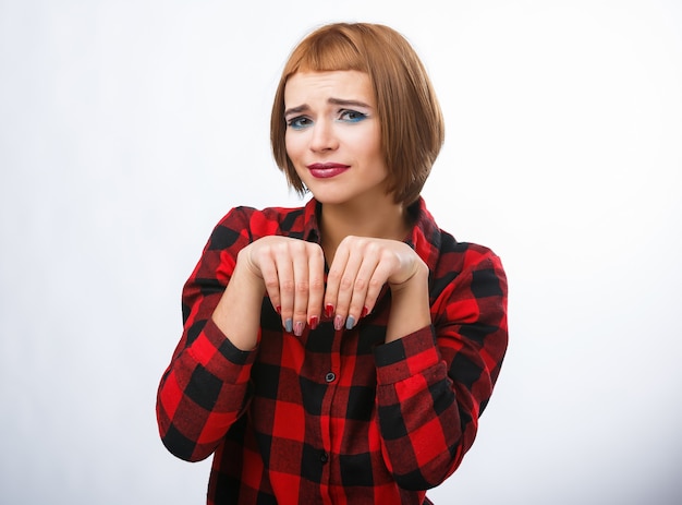 Woman makes bagging sign with hands. Young woman's portraits with different happy emotions. Checkered shirt and red hair. Pitiful emotions.