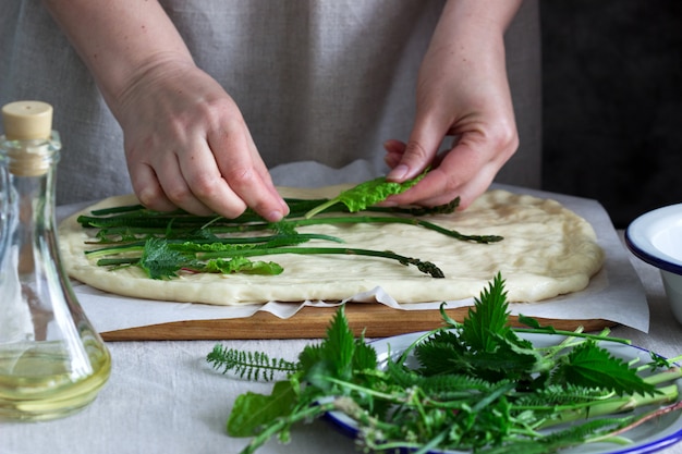 Woman makes focaccia from yeast dough with various herbs. Rustic style.