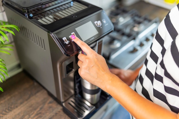 A woman makes fresh flavored coffee with a modern coffee machine in her kitchen