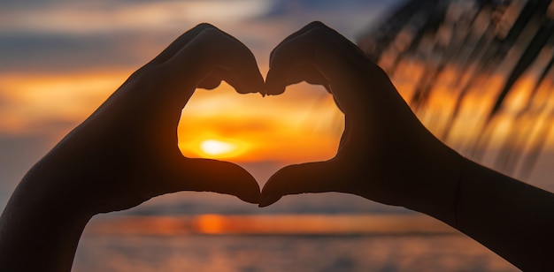 Woman makes heart hands at sunset