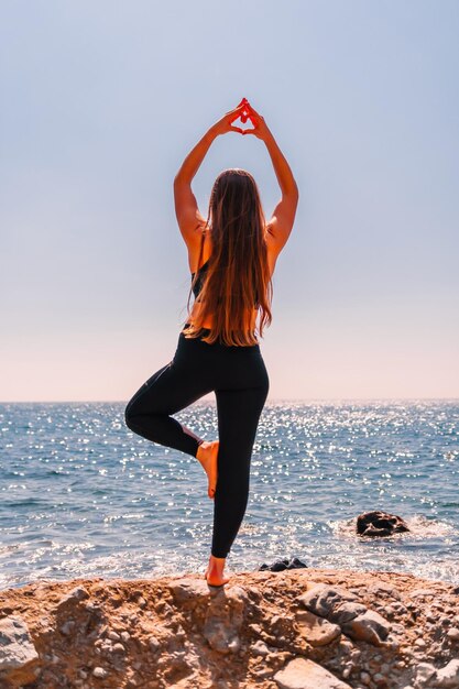 Woman makes heart with hands on beach young woman with long hair fitness instructor stretching