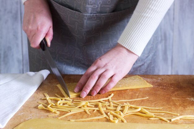 A woman makes homemade noodles from flour, eggs and salt. Rustic style.