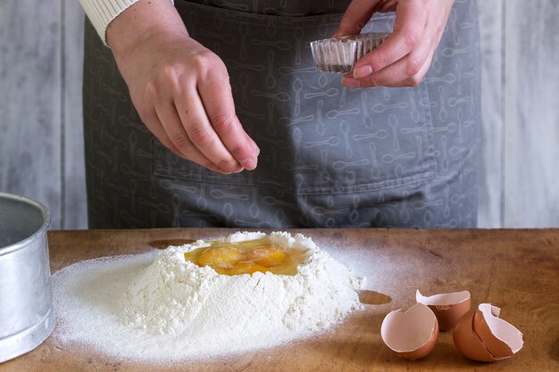 Una donna produce noodles fatti in casa con farina, uova e sale. stile rustico.