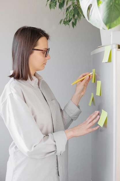 A woman makes notes on colored stickers on the refrigerator a reminder or a note for her husband and