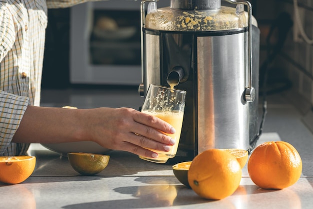 Photo a woman makes orange juice at home in the kitchen with an electric juicer