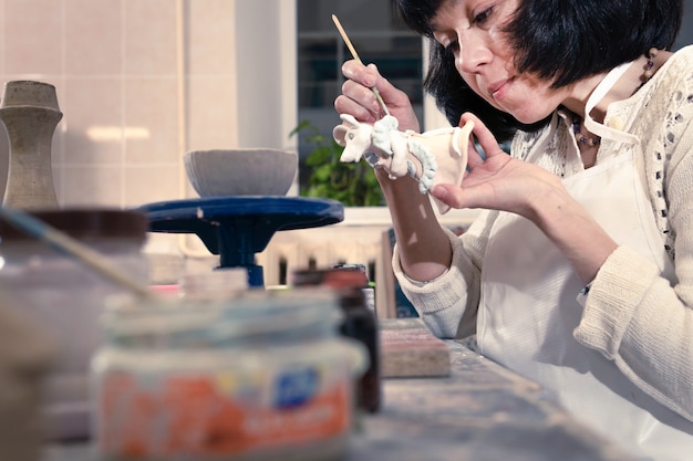 Una donna realizza e dipinge un giocattolo in ceramica fatto di argilla nel laboratorio dello studio.