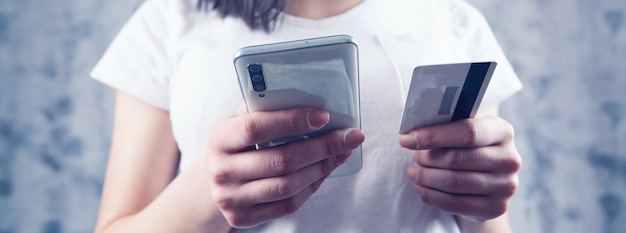 La donna effettua un pagamento per telefono tramite una carta su sfondo grigio