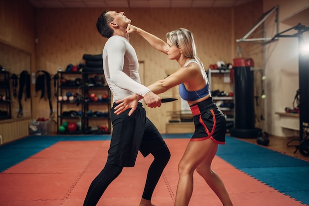 Woman makes punch to the throat, self-defense workout with male personal trainer, gym interior. Female person on training, self defense practice