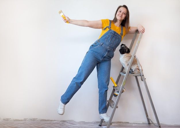 woman makes repairs in her apartment with her pet Funny pet dog sitting on ladder