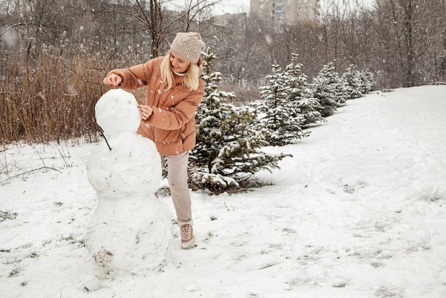 Woman makes a snowman in a city park during a snowfall