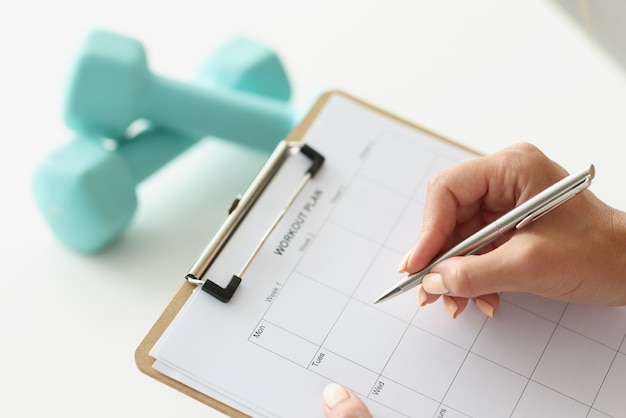 Woman makes workout plan for week next to dumbbells