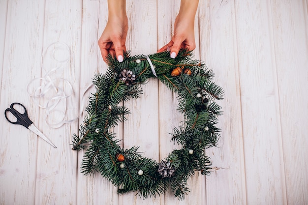 Woman makes a wreath of fir tree branches on the table 