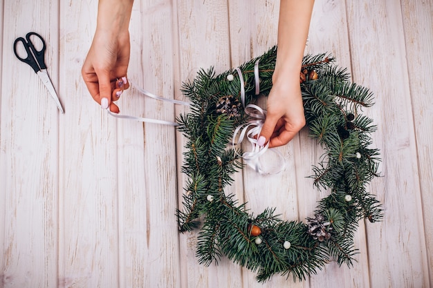 Woman makes a wreath of fir tree branches on the table 