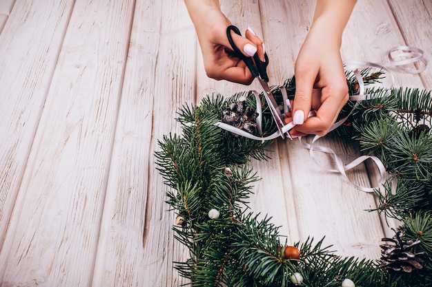 Woman makes a wreath of fir tree branches on the table 