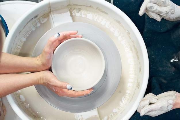 Woman making ceramic pottery, four hands close-up, focus on potters, palms with pottery