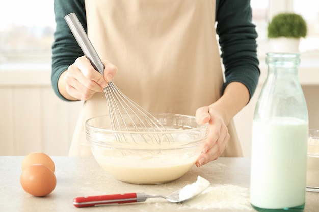 Woman making dough in glass bowl on table in kitchen