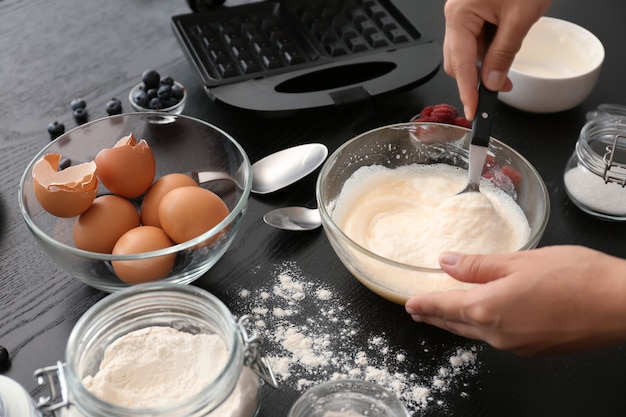 Woman making dough for waffles in kitchen