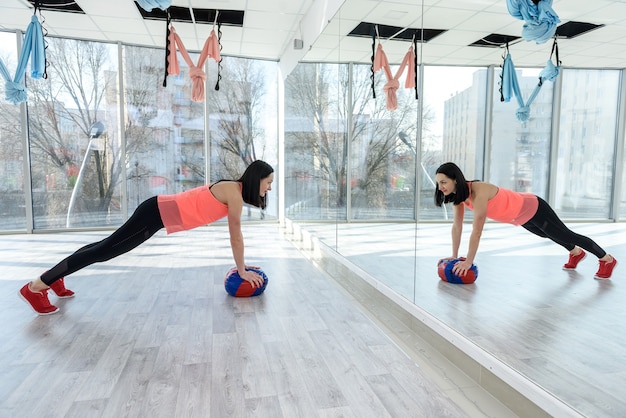 Женщина делает упражнения с мячом перед зеркалом в тренажерном зале