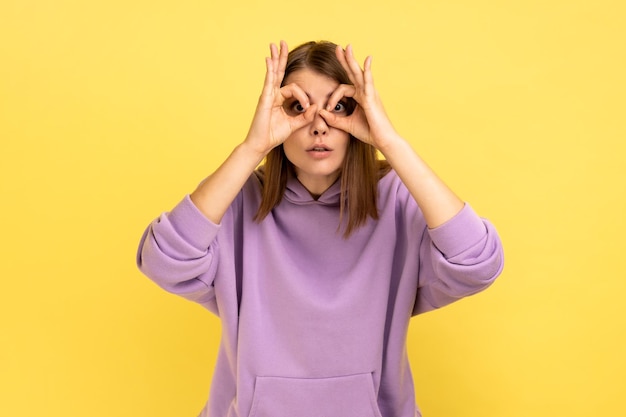 Woman making glasses shape with fingers looking through binoculars hand gesture and expressing shock