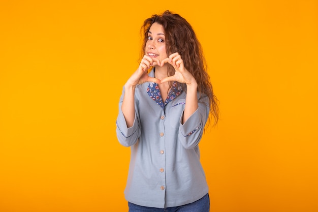 Woman making heart sign with hands on yellow