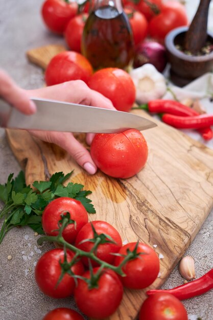 Woman making notch on a tomato on wooden cutting board on grey kitchen concrete or stone table