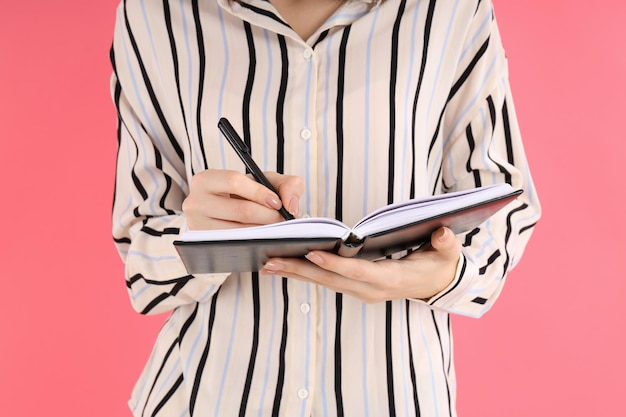 Woman making notes in a notebook on a pink background