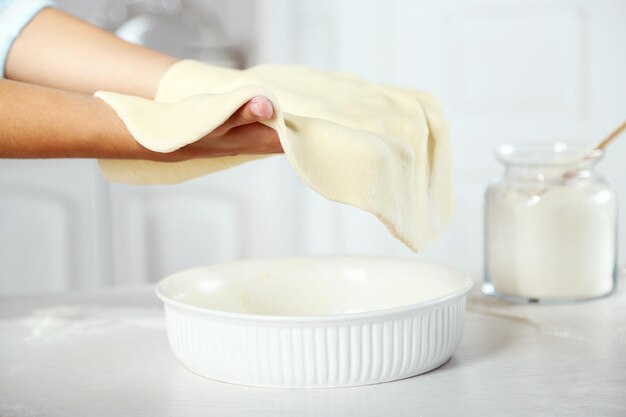 Woman making pie on wooden table on light background