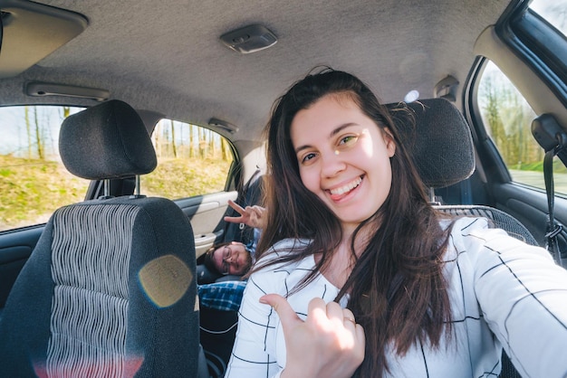 Woman making selfie while driving car with slipping man on backseats. car travel concept