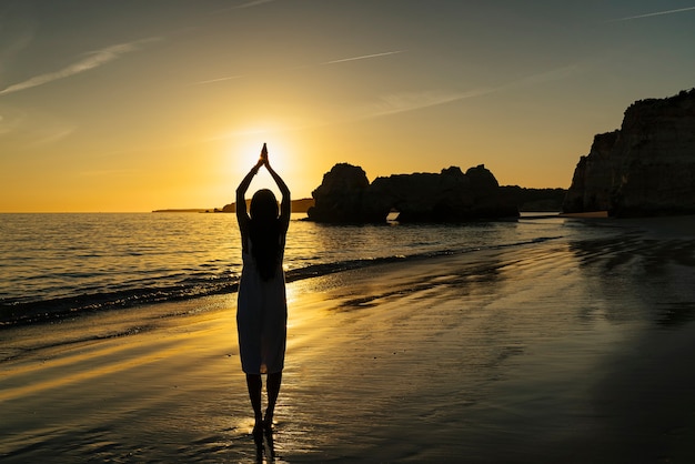 Foto donna che fa shilouette con le mani e il sole al tramonto sulla spiaggia