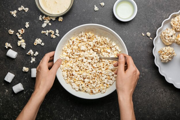 Woman making tasty popcorn balls on dark surface