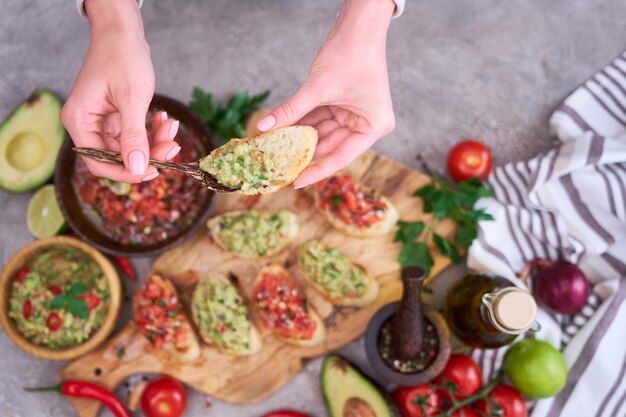 Фото Женщина готовит вкусные закуски из брускетты сальсы и гуакамоле на домашней кухне