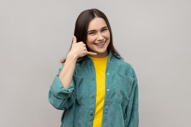 Woman making telephone gesture and smiling playfully waiting for call wants to talk on phone