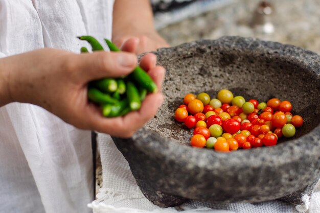 Woman making a traditional Mexican sauce with cherry tomatoes and chilli peppers in a molcajete