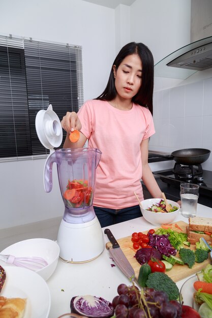 woman making vegetable smoothies with blender in kitchen