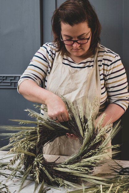 Photo woman making a winter wreath adding dried grasses and seedheads and twigs with brown leaves