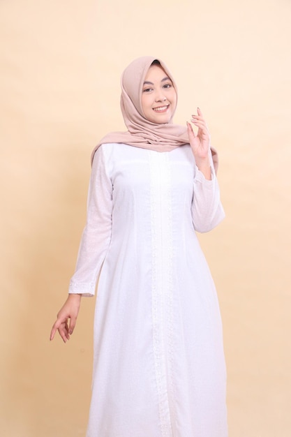 woman malaysia wearing beautiful muslim dress cheerful smile pose hands down and to chest isolated on cream background beauty model studio and fashion concept